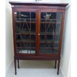 A late Victorian mahogany cabinet-on-stand with a pair of glazed doors, enclosing four shelves,