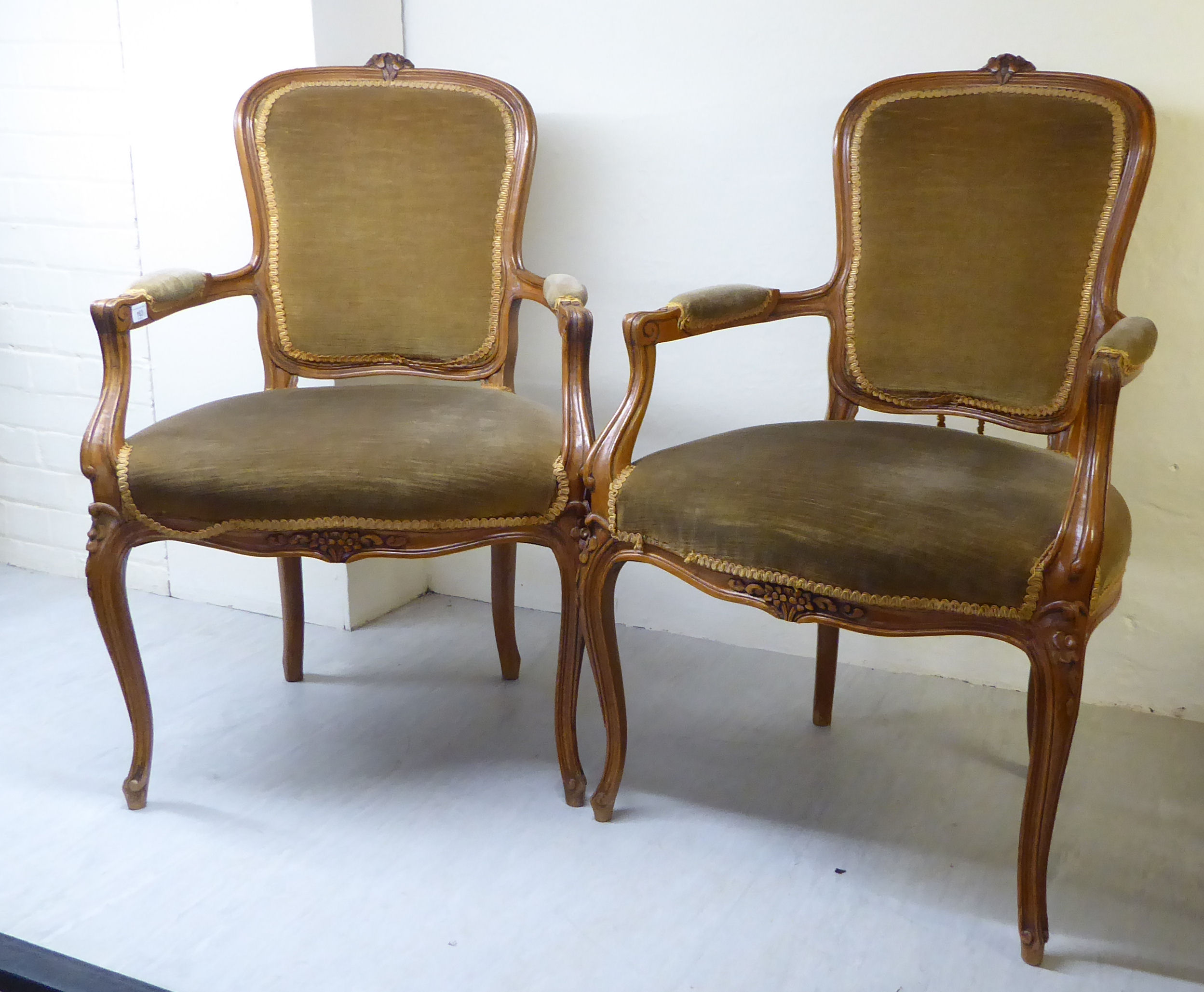 A pair of late 19thC Louis XVI design walnut framed salon chairs, each with a floral carved crest,