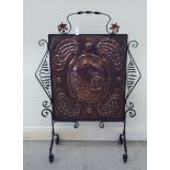 An early 20thC wrought iron framed firescreen, set with a Newlyn School copper panel,