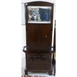 A 1930s oak stickstand, surmounted by a bevelled mirror, over a hinged seat,