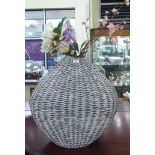 A modern woven cane vase 22''h containing an arrangement of faux flowers and foliage RAB