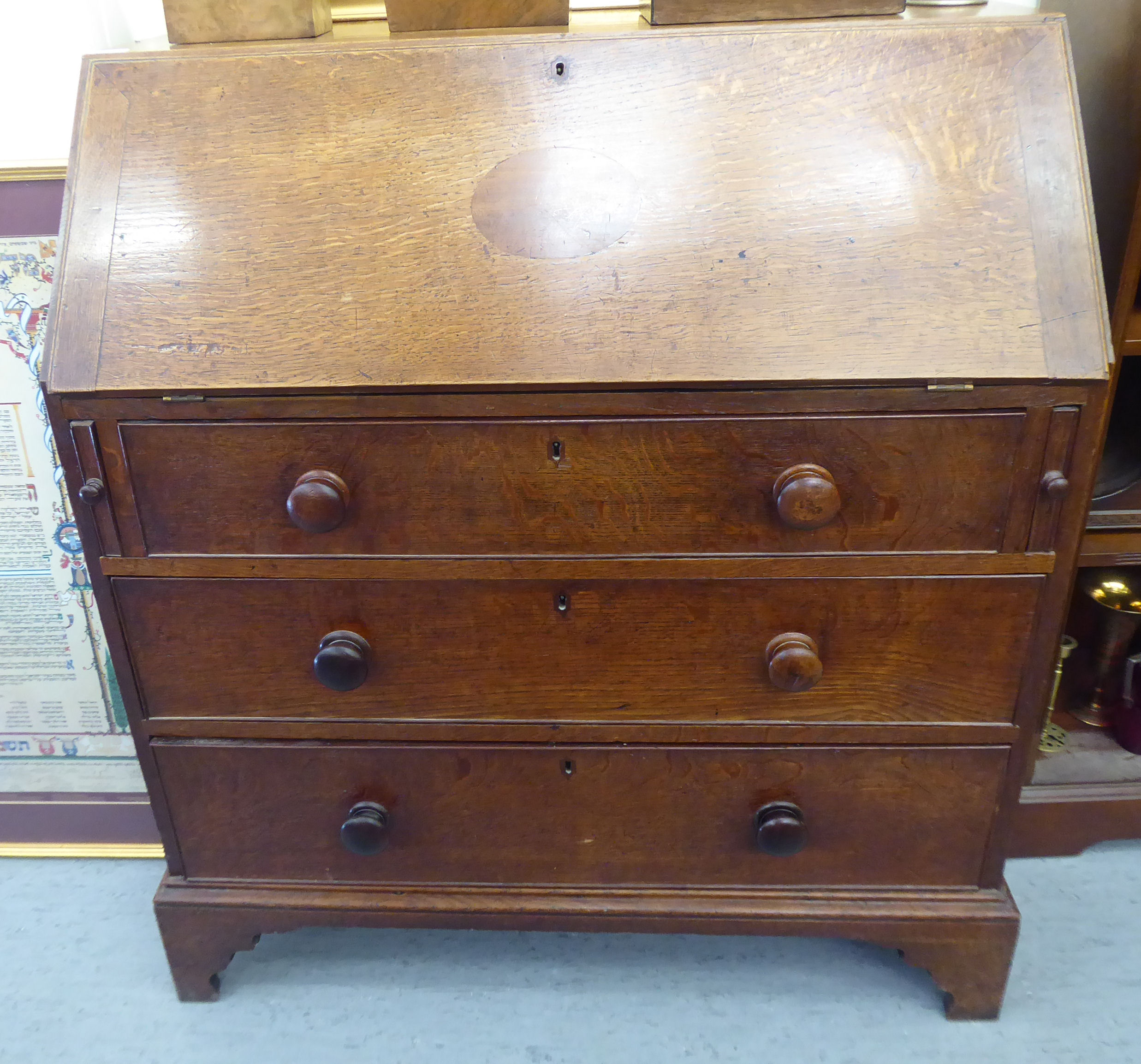 A George III oak bureau, the fall flap over three graduated drawers,