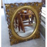 A mid 20thC mirror, the oval bevelled plate set in an ornate,