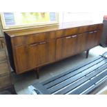 An early 1970s Mcintosh teak sideboard with three frieze drawers, over a central fall flap,
