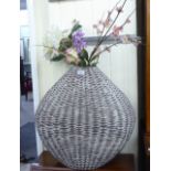A modern woven cane vase 22'h containing an arrangement of faux flowers and foliage CA