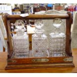 A 1920s oak and rivetted steel mounted table top tantalus, the locking bar securing three squares,