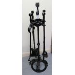 An Arts & Crafts black painted and riveted wrought iron fireside companion,