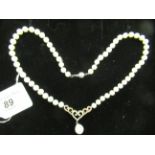 A string of cultured pearls with a bi-coloured 14ct gold twin c-scrolled and heart shaped diamond