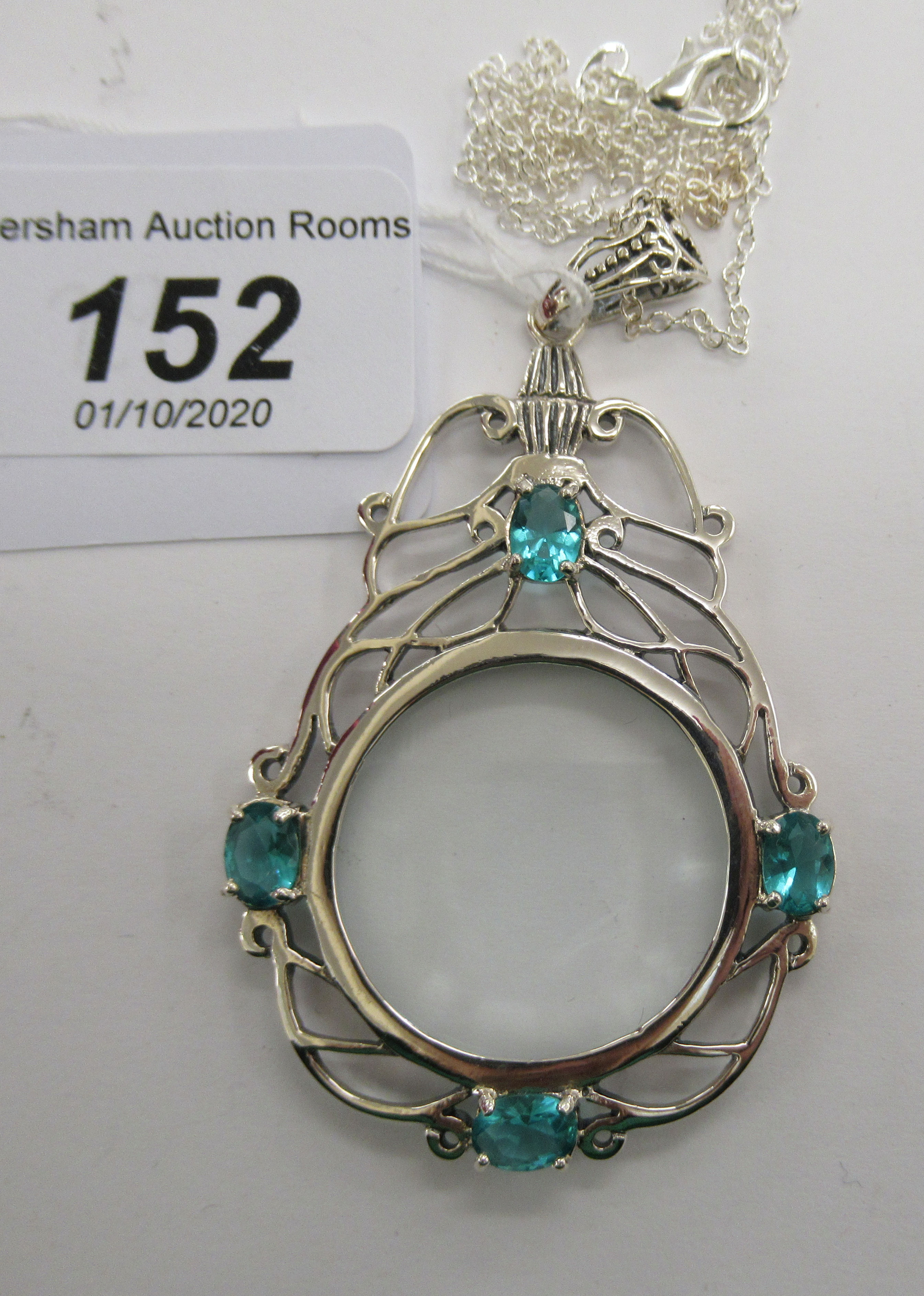 A silver framed magnifying glass pendant, set with blue topaz,