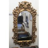 A modern mirror, the arched bevelled plate set in a moulded gilt frame with feathered, floral,