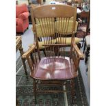 An early 20thC American spindled back open arm chair with a solid seat, raised on turned,