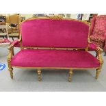 A 20thC gilt gesso framed three person salon settee, upholstered in a bright pink coloured fabric,