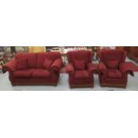 A three piece suite with level backs and scrolled arms, upholstered in maroon fabric,