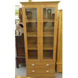 A modern light oak finished cabinet bookcase with a level cornice, over a pair of glazed,