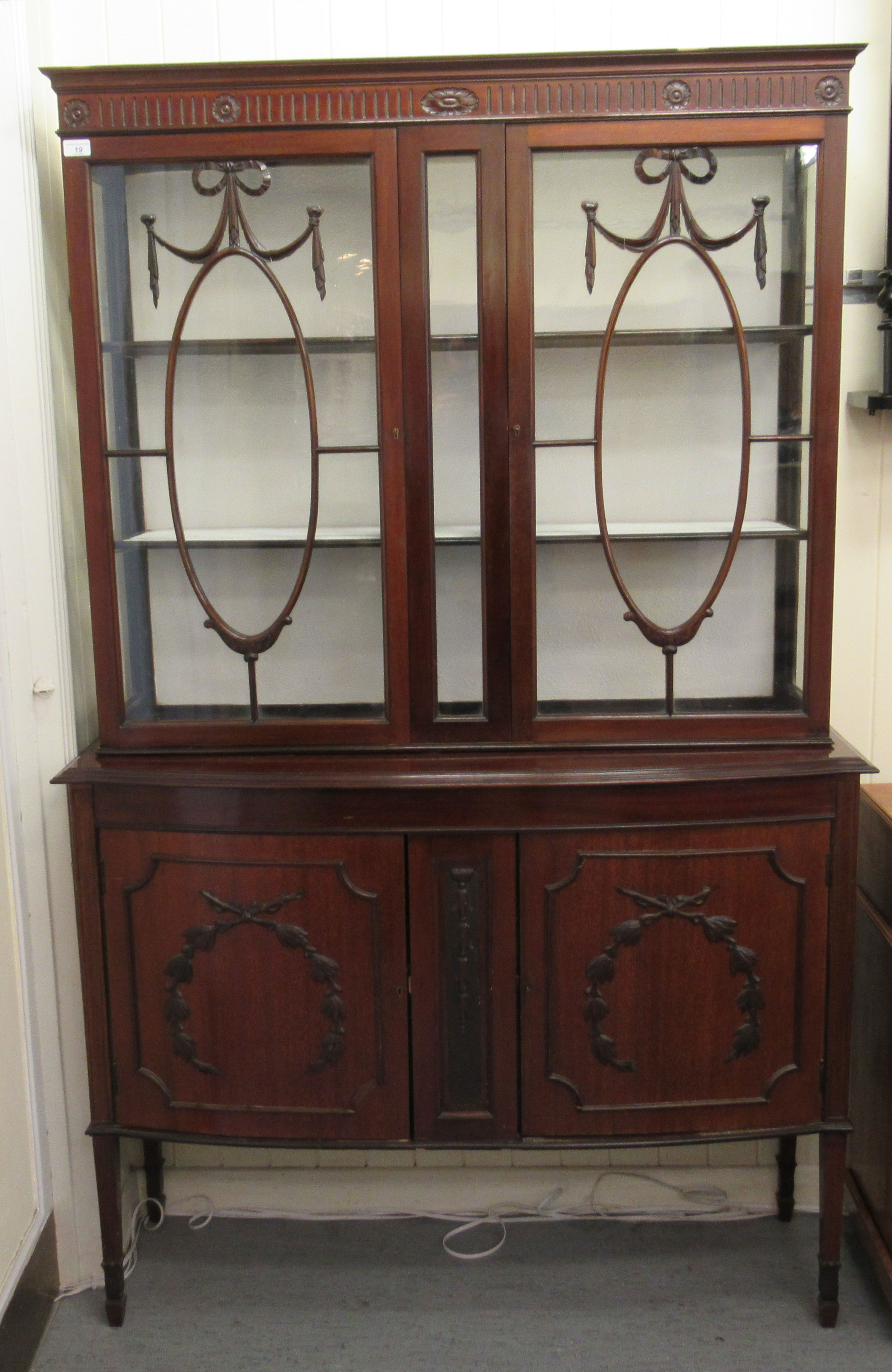 An Edwardian mahogany display cabinet with a pair of glazed doors, over a bow front,