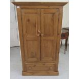 A modern pine wardrobe with a pair of panelled doors, enclosing two short rails,