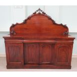 A late Victorian mahogany sideboard, having an arched, foliate and fruit carved panelled back,