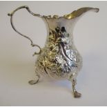 A George II silver cream jug of waisted, bulbous form, embossed with floral designs,