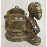 An African tribal art, carved wooden seated male figure, beside a circular, covered pot,