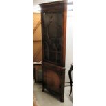 A modern mahogany corner cupboard, the glazed door top enclosing three shelves, over a door,