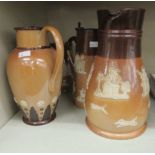 Four Doulton Lambeth and Royal Doulton two tone brown glazed stoneware milk jugs with lids and of