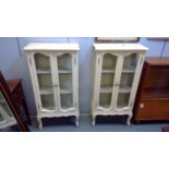 A pair of 20th Century cream painted display cabinets, the shaped top above glazed doors and