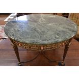 A circular coffee table with green marble top on a brass base with pink cabochons and reticulated