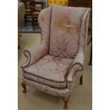 A Georgian style wing back upholstered arm chair, cabriole front supports with pad feet