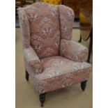 A Georgian style wing back arm chair, turned front supports with castors and foliate upholstery