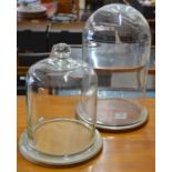 A circular Pyrex glass dome on wooden base, another glass dome with knop finial to/w a G. Klimpt