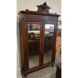 A French mahogany armoire with carved and fluted pediment over a pair of bevelled mirrored doors