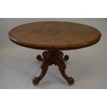 A Victorian oval tilt top breakfast table with burr walnut top raised on heavily carved quad base