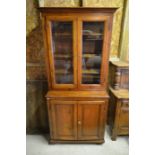 A stained pine bookcase cabinet with glazed doors enclosing three shelves over a pair of panelled