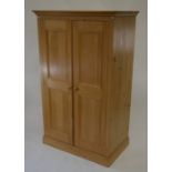 A small pine wardrobe, the pair of panelled doors enclosing shelves and hanging rail, raised on