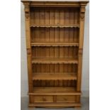 A Continental carved pine open bookcase with four shelves over two drawers raised on bracket feet,