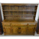 An elm dresser, the wide plate rack with two shelves on a base with three drawers over panelled