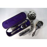 A matched three piece silver-backed brush set with cherub masks