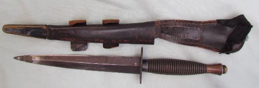 A Commando knife, with a ribbed handle, with a tapering blade in a leather scabbard, 290.