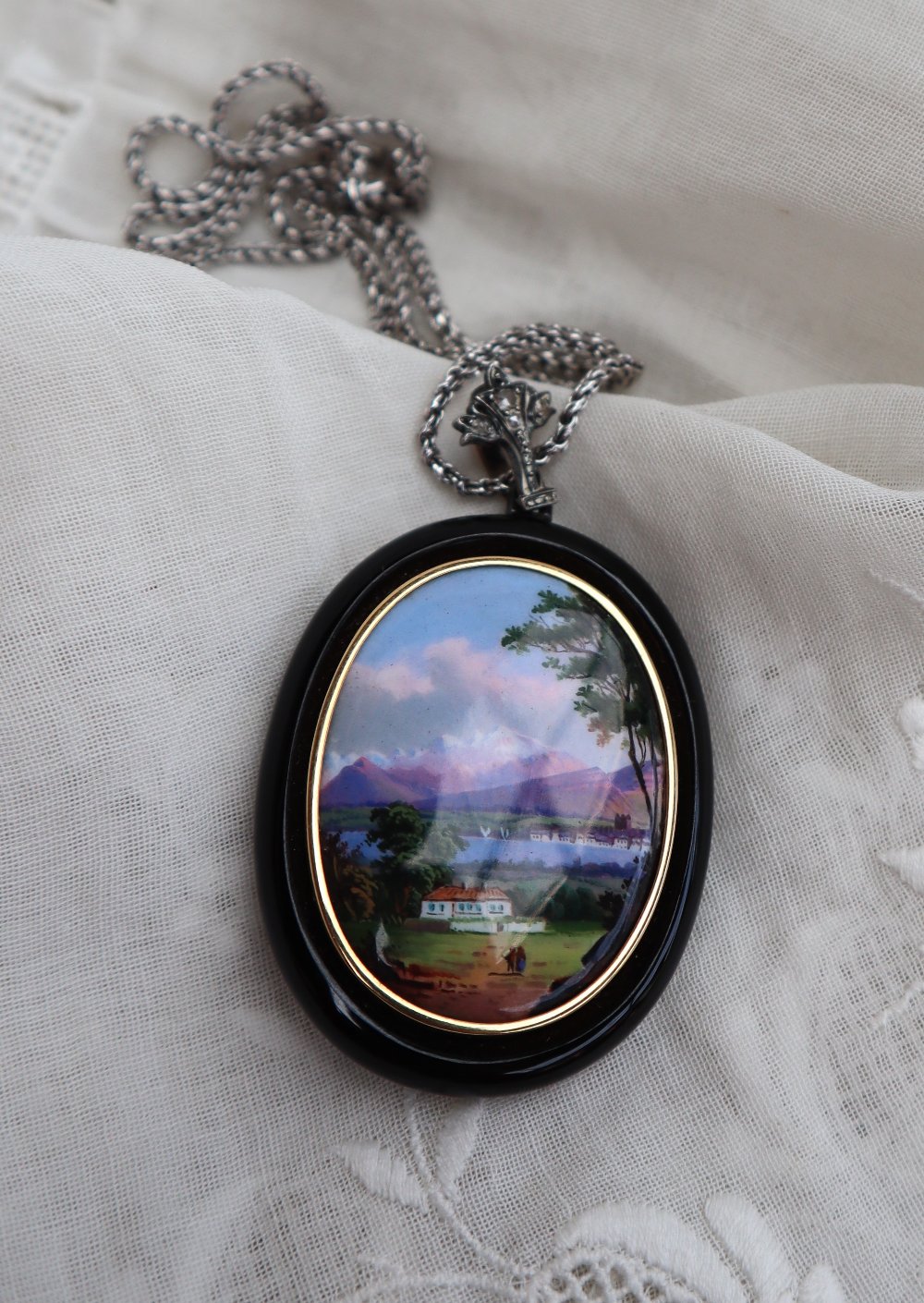 A continental pendant with an oval panel painted with a lake scene with a mountain range beyond,