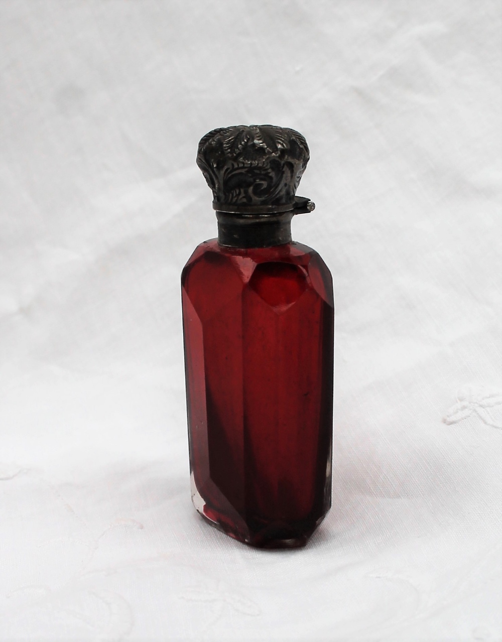 An Edwardian Silver topped and cranberry glass scent bottle, cast with leaves to a faceted body,