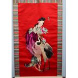 A Japanese silkwork scroll, decorated with a geisha and a crane, to a red ground,