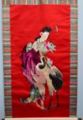 A Japanese silkwork scroll, decorated with a geisha and a crane, to a red ground,