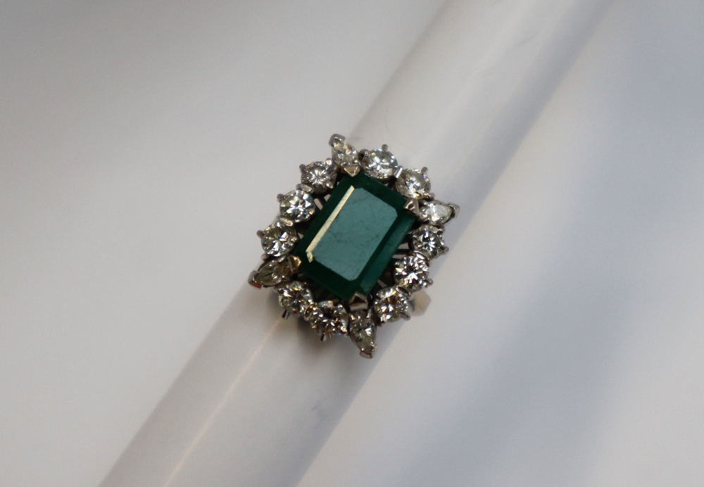 An emerald and diamond cluster ring, the central emerald cut emerald approximately 12mm x 9mm,