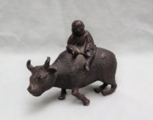 A Chinese white metal figure of a boy riding a water buffalo, patinated to simulate bronze, 10.