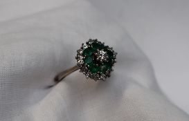 An Emerald and diamond cluster ring, the central round brilliant cut diamond approximately 0.