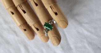 An emerald and diamond ring, the central emerald approximately 7mm x 4mm,