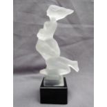 A frosted glass mascot of nude lovers in the style of H Hoffmann, on a black glass plinth,