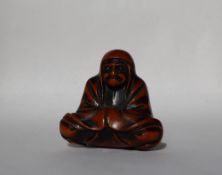 A 19th century carved wooden netsuke in the form of Daruma, seated crosslegged,