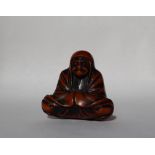 A 19th century carved wooden netsuke in the form of Daruma, seated crosslegged,