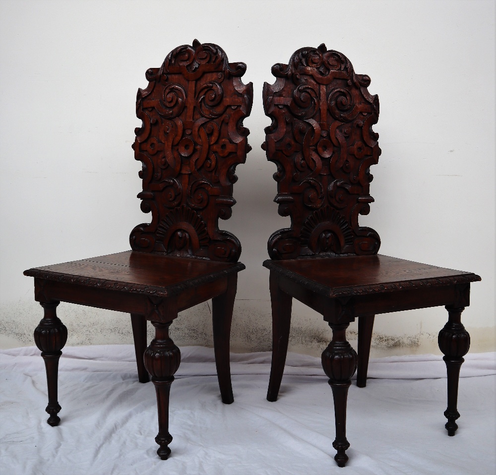 A pair of continental carved oak hall chairs, the back decorated with scrolling leaves and a shell,